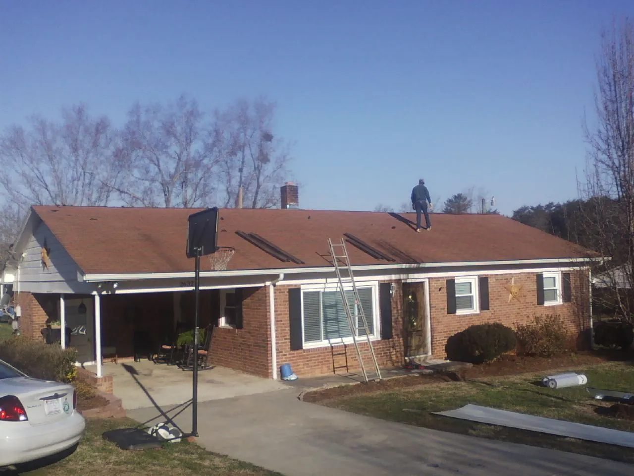 Roofer stripping a shingle roof on a brick ranch before metal panels in Saratoga