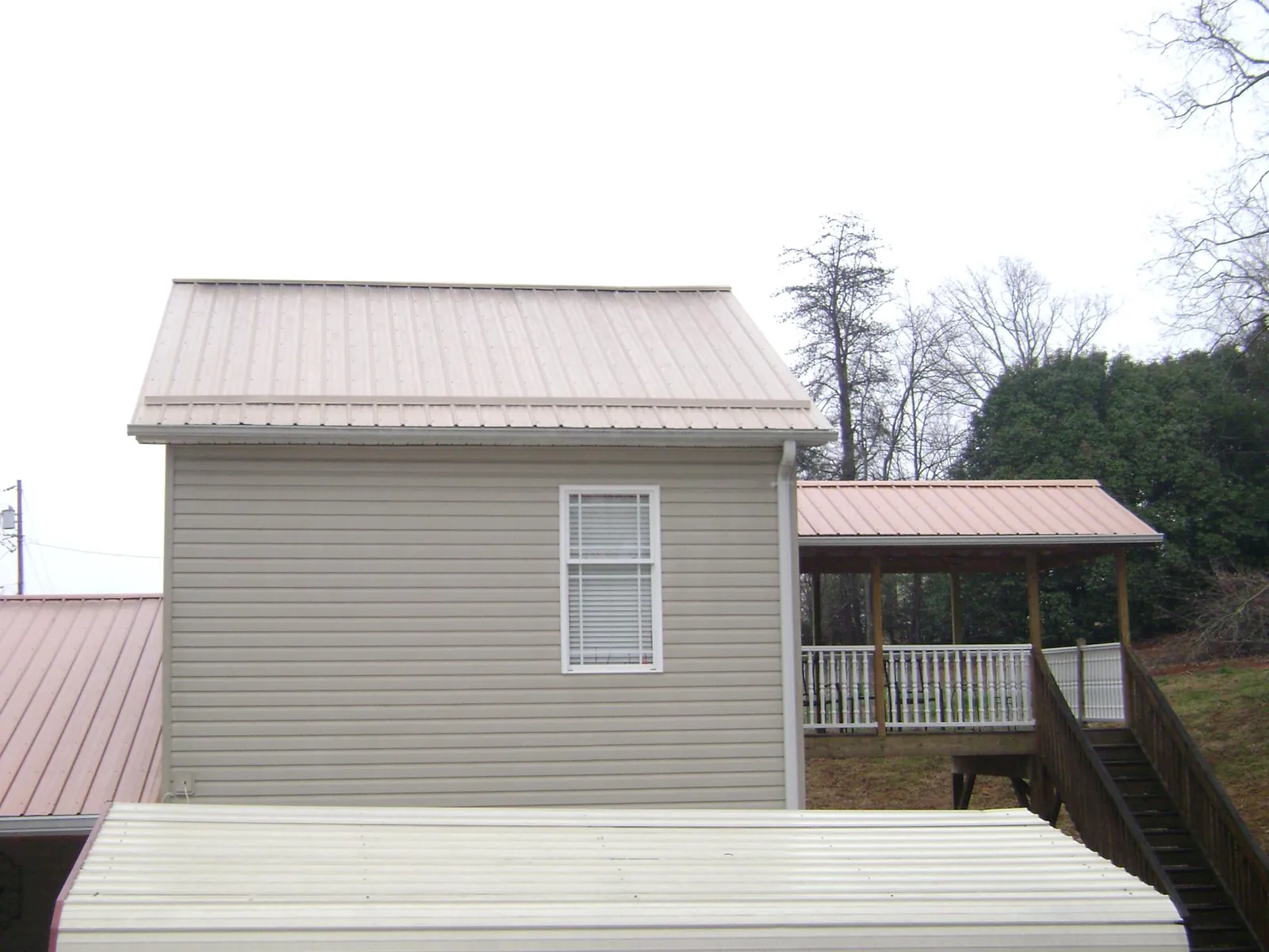 Tan metal roofs on a two story addition and attached porch, from a Roof Replacement job in Saratoga
